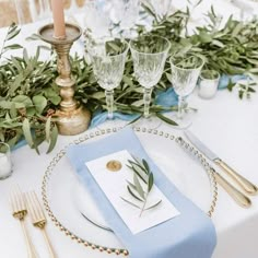 a place setting with silverware, napkins and greenery on the table top