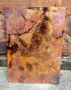 a rusted metal piece sitting next to a brick wall