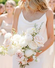 a bride holding a bouquet of white and pink flowers in her hands with other bridesmaids behind her