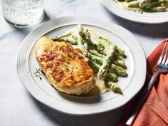 two white plates topped with chicken and asparagus next to a glass of water