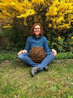 a woman sitting on the ground with a ball in front of her and yellow flowers behind her