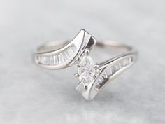 a white gold engagement ring with two baguettes on each side and a diamond set in the middle