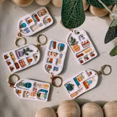 four keychains with different designs on them sitting next to some shells and plants