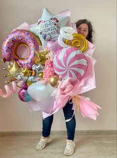 a woman is holding a large bouquet of balloons and other items in front of her