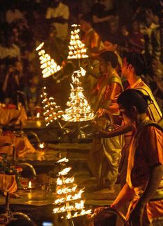 people standing around with lit candles in their hands and looking at the water that is running through them