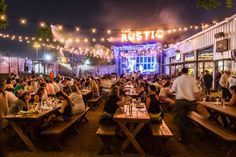 many people are sitting at picnic tables in front of a building with lights strung over it