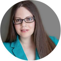 a woman with glasses is looking into the camera while wearing a blue shirt and green blazer