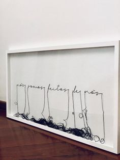 a white framed artwork with writing on the wall and wood flooring in front of it