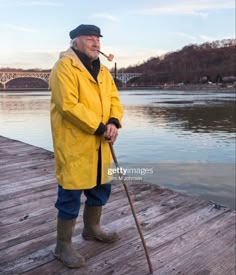 an old man standing on a dock with a pipe in his mouth and wearing a yellow raincoat