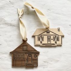 two wooden ornament shaped like houses on a white surface with a ribbon hanging from the front