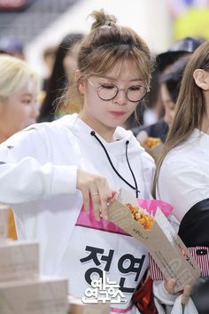 two young women standing next to each other while holding food in their hands and looking at something