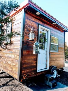 the tiny house is made out of wood and has a white door, windows, and window sill