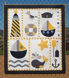 a quilted wall hanging on a fence with boats and lighthouses in the background