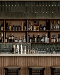 the bar is full of liquor bottles and empty glasses on the shelves behind the stools