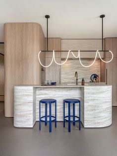 a kitchen with two blue stools next to a counter top and an island in the middle