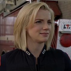 a woman with blonde hair is standing in front of a fire truck and looking off into the distance