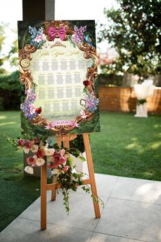 an easel with a wedding seating chart on it in front of some grass and flowers