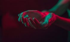 two hands holding something in the dark with red and green light coming from behind them