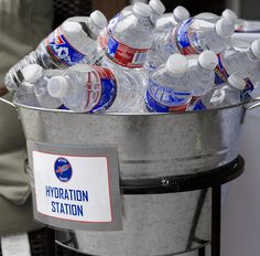 a bucket full of bottled water sitting on top of a metal table next to a person