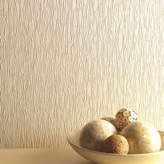 three balls in a white bowl on a table next to a wallpapered background