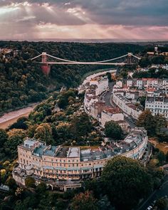 an aerial view of a city and bridge in the distance, with trees surrounding it