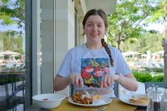 a woman sitting at a table with plates of food in front of her and smiling