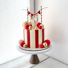 a red and white striped cake on a stand with two small figurines sitting on top