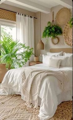 a white bed sitting in a bedroom next to a window filled with potted plants