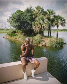 a man sitting on a wall talking on a cell phone next to a body of water