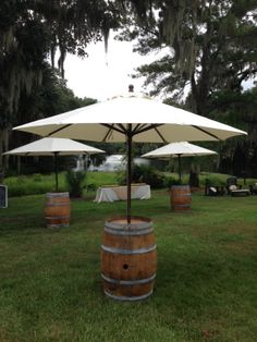 two umbrellas and some barrels in the middle of a yard with tables set up behind them