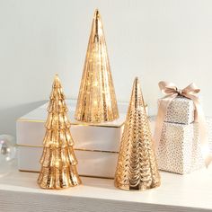 three gold christmas trees sitting on top of a white shelf next to boxes and presents