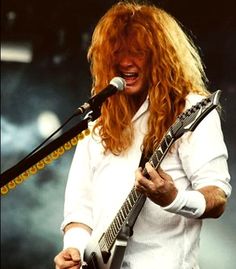 a man with long red hair holding a guitar in front of a microphone on stage