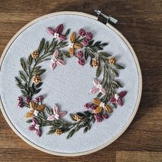 a white embroidery hoop with pink and yellow flowers on it sitting on top of a wooden table