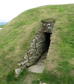 an old stone structure with grass growing on the side and water in the back ground