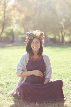 a pregnant woman sitting in the grass wearing a flower crown