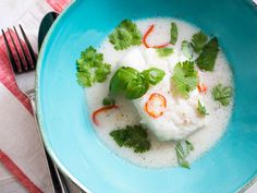 a blue bowl filled with soup and garnished with cilantro, limes, and red peppers