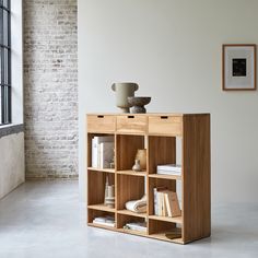 a wooden shelf with books and vase on top in front of a brick wall next to a window