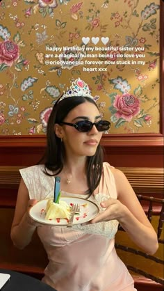 a woman wearing sunglasses holding a plate with food on it in front of a sign