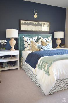 a bedroom with blue walls and white bedding, two lamps on either side of the bed