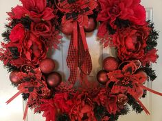 a wreath with red flowers and ornaments hanging on the front door