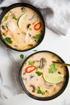 two black bowls filled with soup on top of a white table