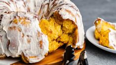 a bundt cake with icing sitting on top of a wooden cutting board next to a white plate