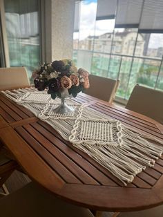 a wooden table topped with a vase filled with flowers next to a window covered in blinds