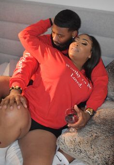 a man and woman laying in bed with their arms around each other holding wine glasses