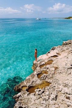 a person standing on the edge of a cliff looking out at the blue water and land