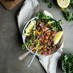 a salad in a bowl on top of a table with lemons and other vegetables