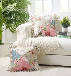 a white couch with pink and blue pillows on it next to a potted plant