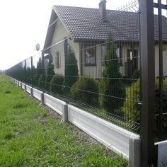 a house behind a wire fence in front of a green field with grass and bushes