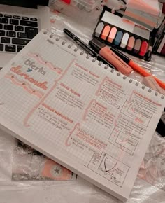 an open notebook sitting on top of a table next to a keyboard and some markers