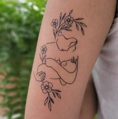 a woman with a tattoo on her arm holding a baby in the middle of flowers